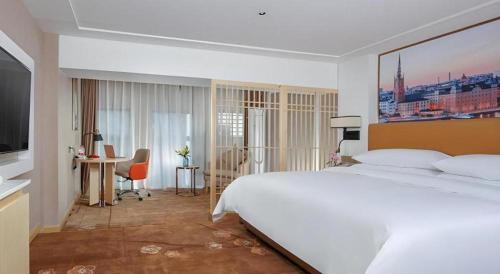 a bedroom with a large white bed and a desk at Vienna Hotel Chengdu Exhibition Center In Time City in Chengdu