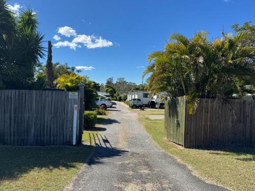 a fence and a driveway with a gate and palm trees at Bushchooks Travellers Village in Bororen