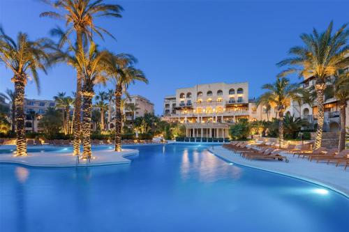 a resort swimming pool with palm trees and a building at Kempinski Hotel San Lawrenz in San Lawrenz