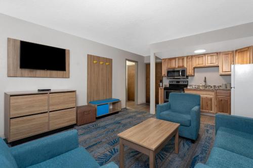 a living room with blue chairs and a kitchen at Days Inn and Suites by Wyndham Downtown Missoula-University in Missoula