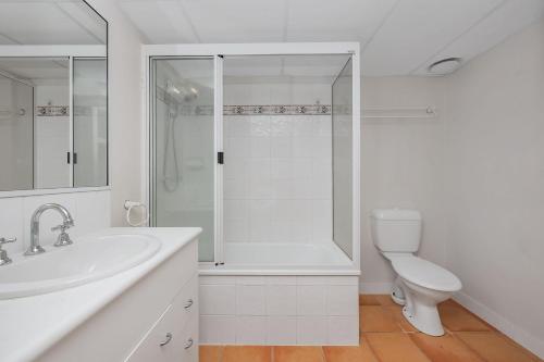 a white bathroom with a shower and a toilet at Steps from The Strand 2BR & 2BA Riveria Retreat Pool & Castle Hill Views in North Ward