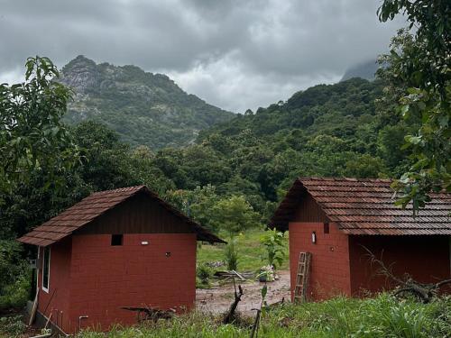 two buildings in a field with mountains in the background at Jungle Homes in Kollengode