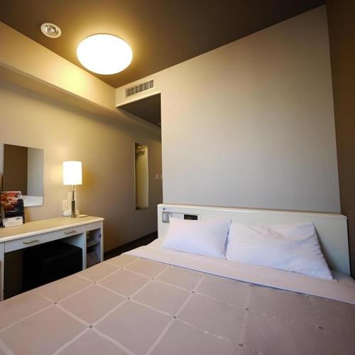 a room with a bed and a desk with a lamp at Hotel Route Inn Kitamatsudo Ekimae in Kashiwa