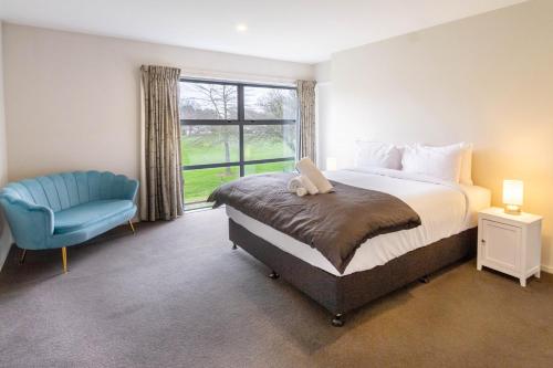 a bedroom with a bed and a blue chair and a window at The Willows Parkside Retreat in Christchurch