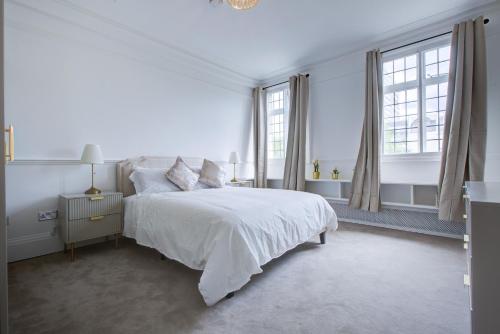 a white bedroom with a bed and two windows at London Baker Street Apartment in London