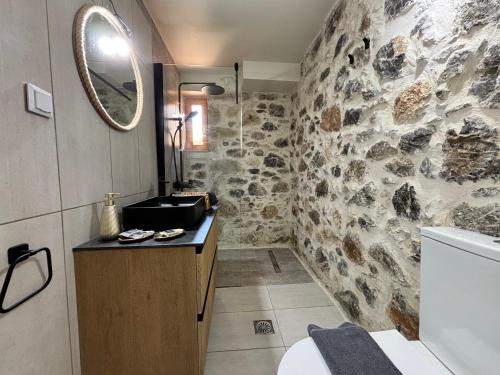a bathroom with a stone wall with a sink and a mirror at Erofili Traditional House in Pómbia