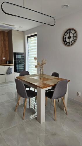 a dining room table with chairs and a clock on the wall at Moderný apartmán v Bobrov s veľkou terasou 1 in Bobrów
