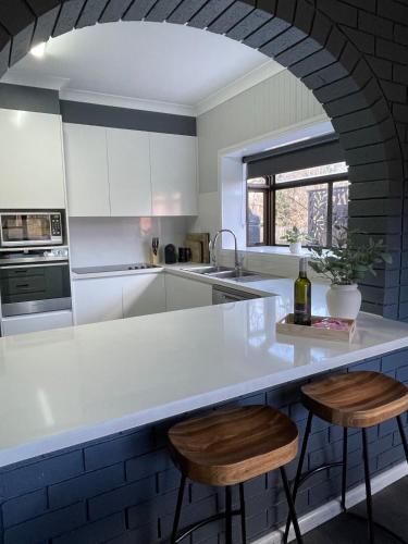 Una cocina con una encimera blanca y dos taburetes. en The Kookaburra house in Moss Vale 5Br Pet friendly, en Moss Vale