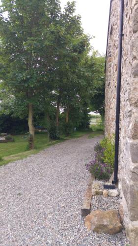 a stone building with a pole next to a gravel road at The Barn at Cae Bach in Gwalchmai
