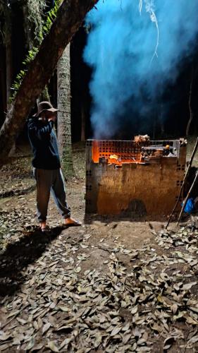a man standing in front of a grill with smoke at Cabana de pesca e lazer Represa Usina Mafra sc in Mafra