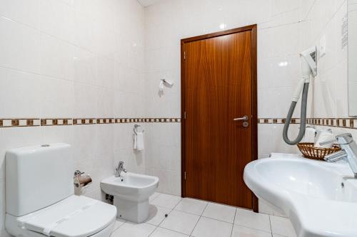 a white bathroom with a toilet and a sink at Hotel La Fontaine in Esmoriz