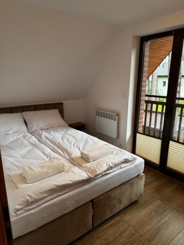 un lit blanc dans une chambre avec une grande fenêtre dans l'établissement Ceglana Przystań - Apartamenty i Domek Pogorzelica, à Pogorzelica