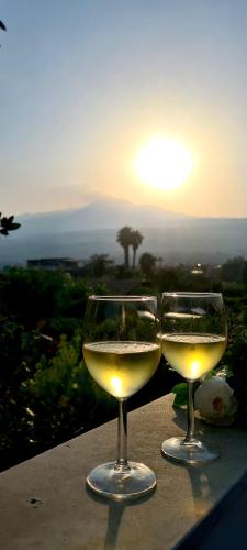 two glasses of white wine sitting on a ledge with the sunset at La mansardina sul mare - Mascali in Mascali
