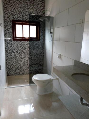 a bathroom with a toilet and a sink and a window at Casa geminada com piscina exclusiva in Arroio do Sal