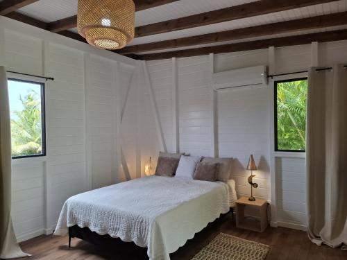 a bedroom with a bed with white sheets and two windows at Bungalow cocon des alizés in Les Abymes