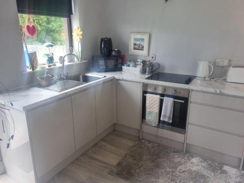 a kitchen with white cabinets and a sink and a window at Cistin Bheag Áine in Ballygawley