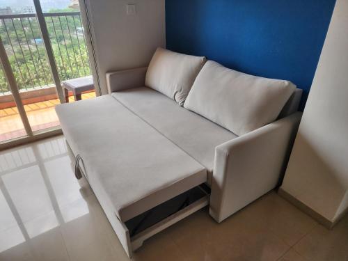 a small white couch in a room with a window at Luxury AC 2BHK Full Furnished with Sunrise View, Hill View, Pool, Kitchen, Ergonomic Workstation in Hinjewadi
