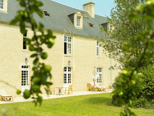 a large brick building with a table and chairs at Hôtel Le Manoir De Mathan Crépon à la campagne 5 mn d'Arromanches et 10 mn de Bayeux in Crépon
