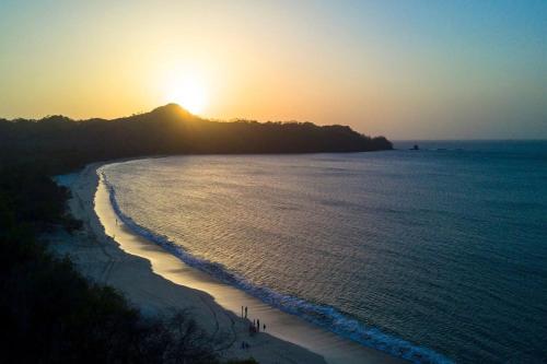 a sunset on a beach with the sun setting over the ocean at The Luxury Condo at Reserva Conchal, Great Beach in Playa Conchal