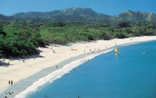 a group of people on a beach with a sailboat at The Luxury Condo at Reserva Conchal, Great Beach in Playa Conchal