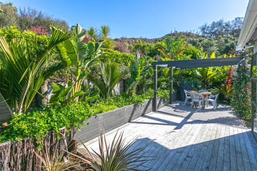 un patio con mesa y sillas en un jardín en Hahei Beach Dolphin cottage, en Hahei