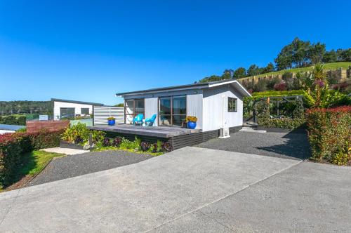 Una pequeña cabaña blanca con un porche y una casa. en Hahei Beach Dolphin cottage, en Hahei