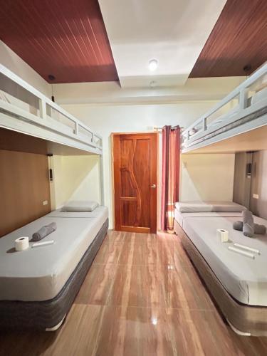 two beds in a room with wooden floors and a door at Baybay Hostel in Siquijor