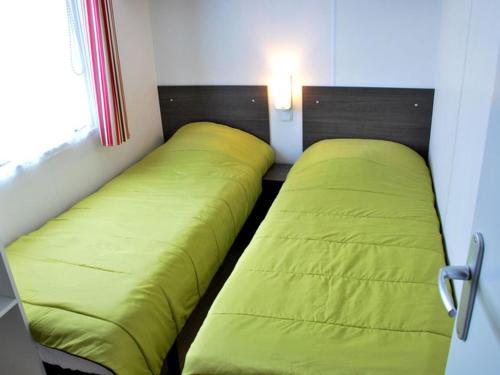 two beds in a small room with green sheets at Mobil home confortable avec terrasse pour 6 personnes - API-1-52-304 in Brétignolles-sur-Mer