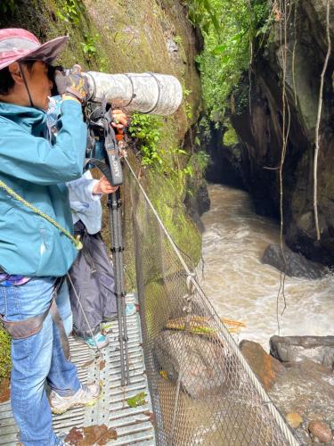 a man with a camera on a bridge over a river at Cabaña Manantial del Turpial in Jardin