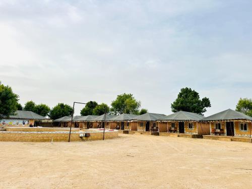 a group of wooden buildings with roofs on a dirt field at The Desert Resort Jaisalmer in Jaisalmer