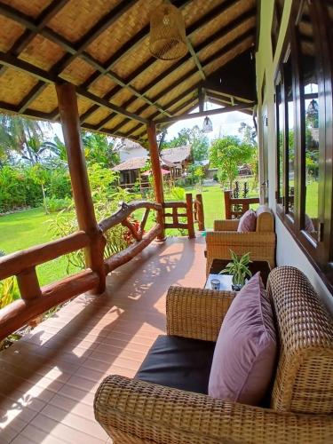 a covered porch with wicker chairs and tables at Sumatra Cheeky Monkeys Villa, Trekking and Tours in Bukit Lawang