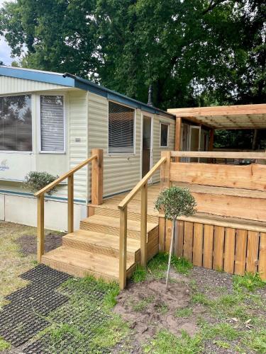 a house with a wooden staircase next to a fence at Heerlijke ruime stacaravan met overdekte veranda en omheinde tuin ''Casa Elvina'' in Eext