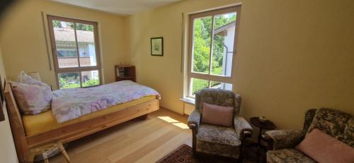 a bedroom with a bed and a chair and two windows at Grünoase vor den Toren Salzburgs in Freilassing