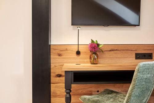 a vase of flowers on a desk with a tv at Hotel Auf der Gsteig GmbH in Lechbruck
