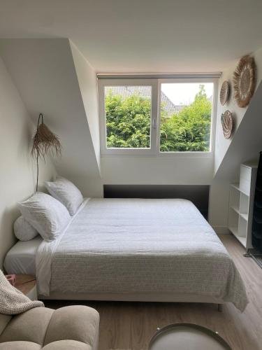 a white bedroom with a bed and a window at Appartement Buissant des Amorie! in Castricum