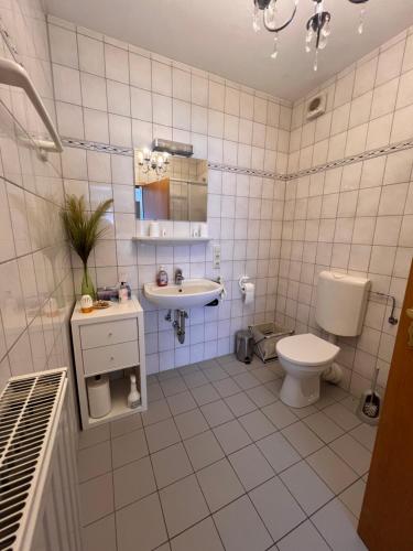 a white tiled bathroom with a toilet and a sink at Ferienwohnung am Nürburgring in Siebenbach