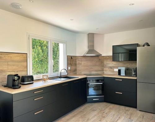 a kitchen with black cabinets and a large window at Logement indépendant avec piscine privée in Penta-di-Casinca