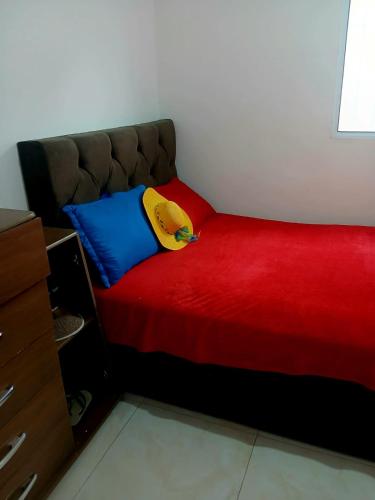 a bed with a red blanket and a yellow pillow at Apartamento na praia 2 qt com quintal e churrasqueira in Itanhaém