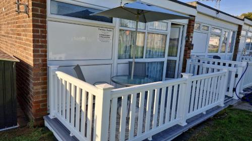 a white porch with a table and an umbrella at Park view chalet in Hemsby