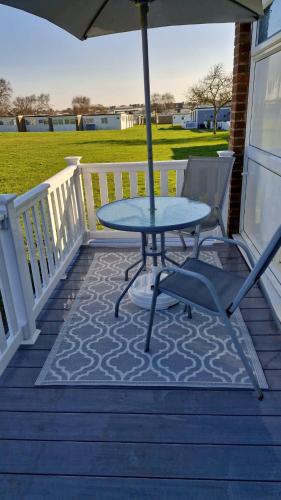 a table and chairs on a porch with an umbrella at Park view chalet in Hemsby