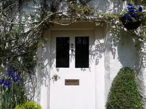 a white door on a white house with flowers at Tracebridge Cottage B&B in Stawley
