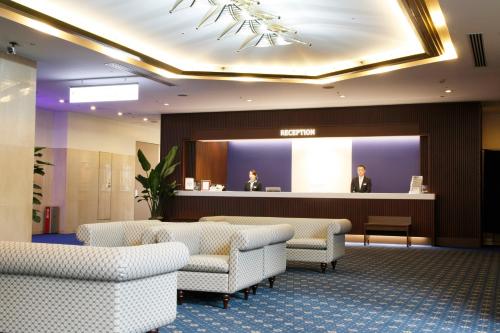 a lobby with a waiting room with chairs and a man on a screen at Rembrandt Hotel Tokyo-Machida in Machida