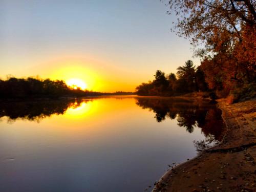 a sunset over a river with the sun setting at The River Cabin in Mauston