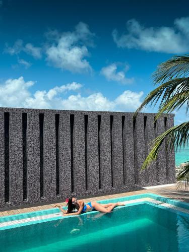 a woman laying on the side of a swimming pool at Nest by Hawks Hotels Kamadhoo Baa Atoll in Kamadhoo