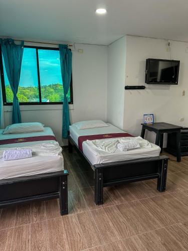 two beds in a room with a tv and a table at HOTEL COLONIAL santorini colombiano in Doradal