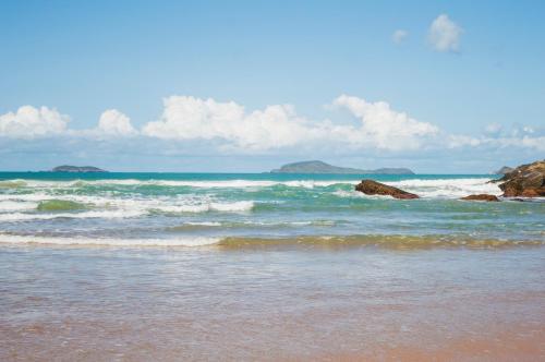 a beach with waves and rocks in the ocean at Apartamento Jardim Geribá in Búzios