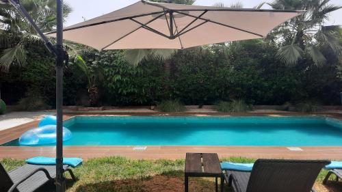 a pool with an umbrella and two chairs and a table at Villa Roseaux heated pool Marrakech in Najem
