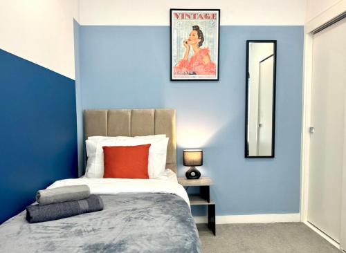 ein blaues Schlafzimmer mit einem Bett und einem Spiegel in der Unterkunft Contemporary Designer 2 Bed Apartment, Free Parking, Gym, Yoga & Cinema Room in Bedford