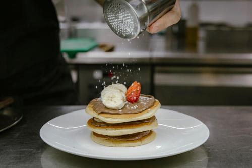 a person is sprinkling powdered sugar on a stack of pancakes at Cugo Gran Macina Malta in Senglea