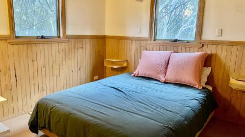 a bedroom with a bed with two pillows and two windows at Tanglewood in Dinner Plain